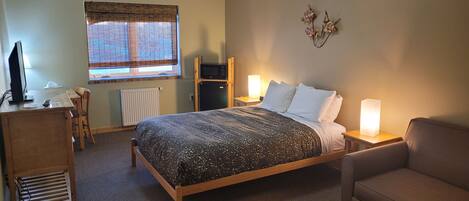 Een hotelkamer met een bed, een bureau, een stoel, een magnetron en een lamp.