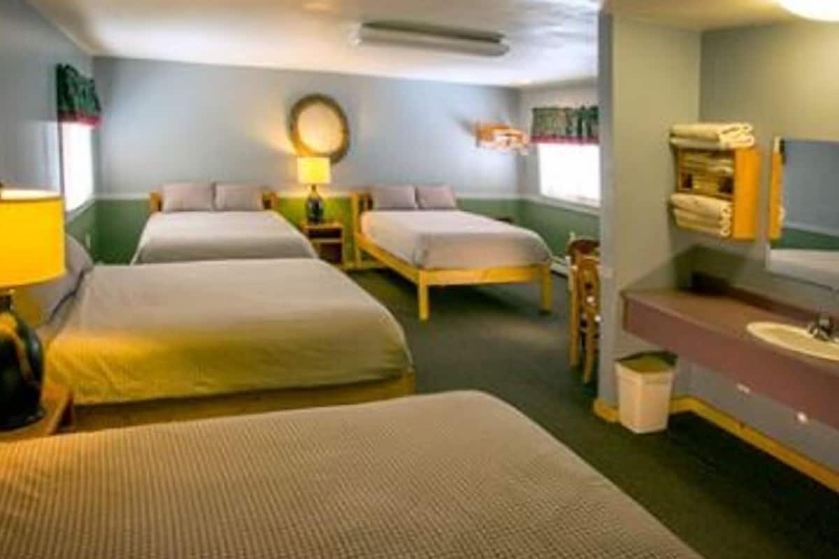 Ein Hotelzimmer mit zwei Einzelbetten, einem Nachttisch mit Lampe, einem kleinen Tisch mit Stuhl, einem Badezimmer mit Waschbecken und Spiegel sowie einem Handtuchhalter an der Wand.