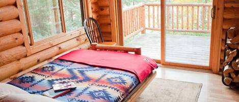 A log cabin bedroom with a bed, a chair, and a view of the deck.