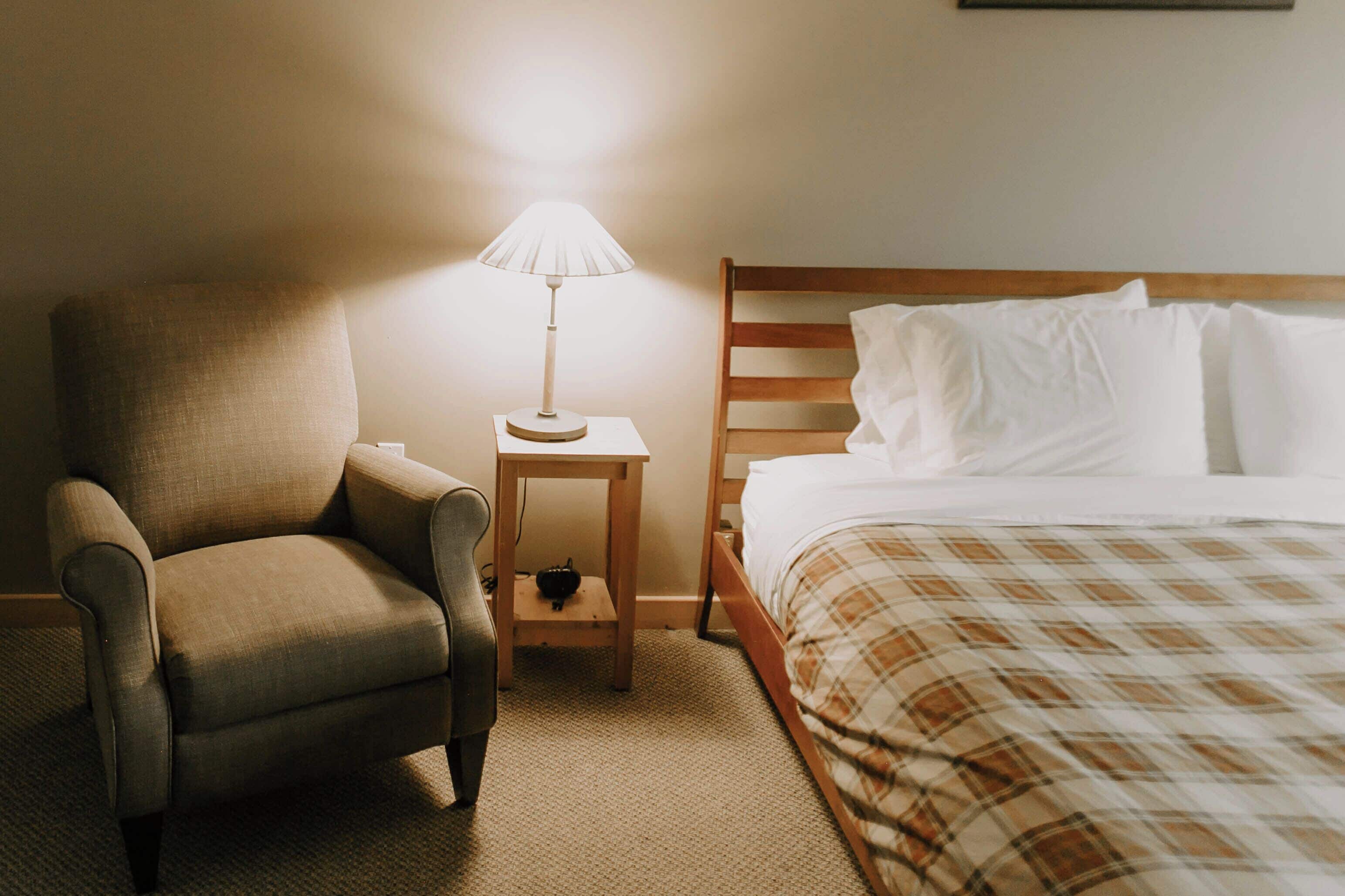 A hotel room with a single bed, a chair, a nightstand with a lamp, and a small table.