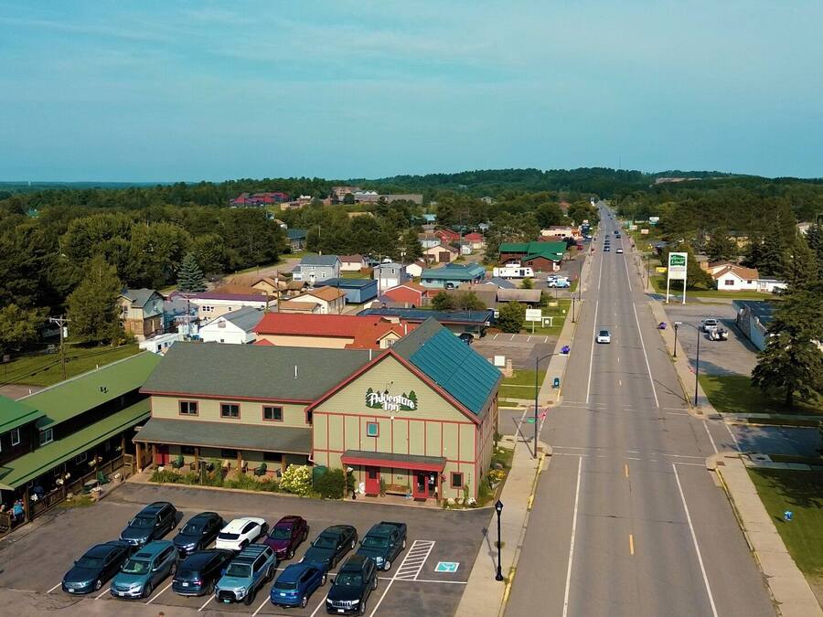An aerial view of a town with a prominent building labeled "Adventure Inn" in the foreground, featuring a parking lot with several cars.