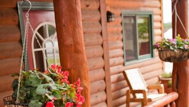Uma cabana de madeira com um deck de madeira, um cesto de flores pendurado e uma cadeira.
