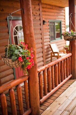 Une cabane en bois avec une terrasse en bois, une jardinière suspendue et une chaise.