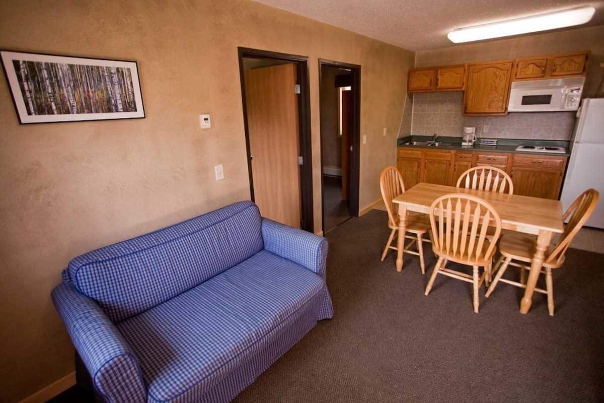 Ein kompakter Wohnraum mit einem blau karierten Sofa, einem Holzesstisch mit Stühlen, einer Küchenzeile mit Holzschränken und einem gerahmten Bild an der Wand.