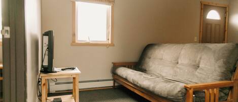 A room with a wooden sofa, a small wooden table with a computer, and a window with a blind.