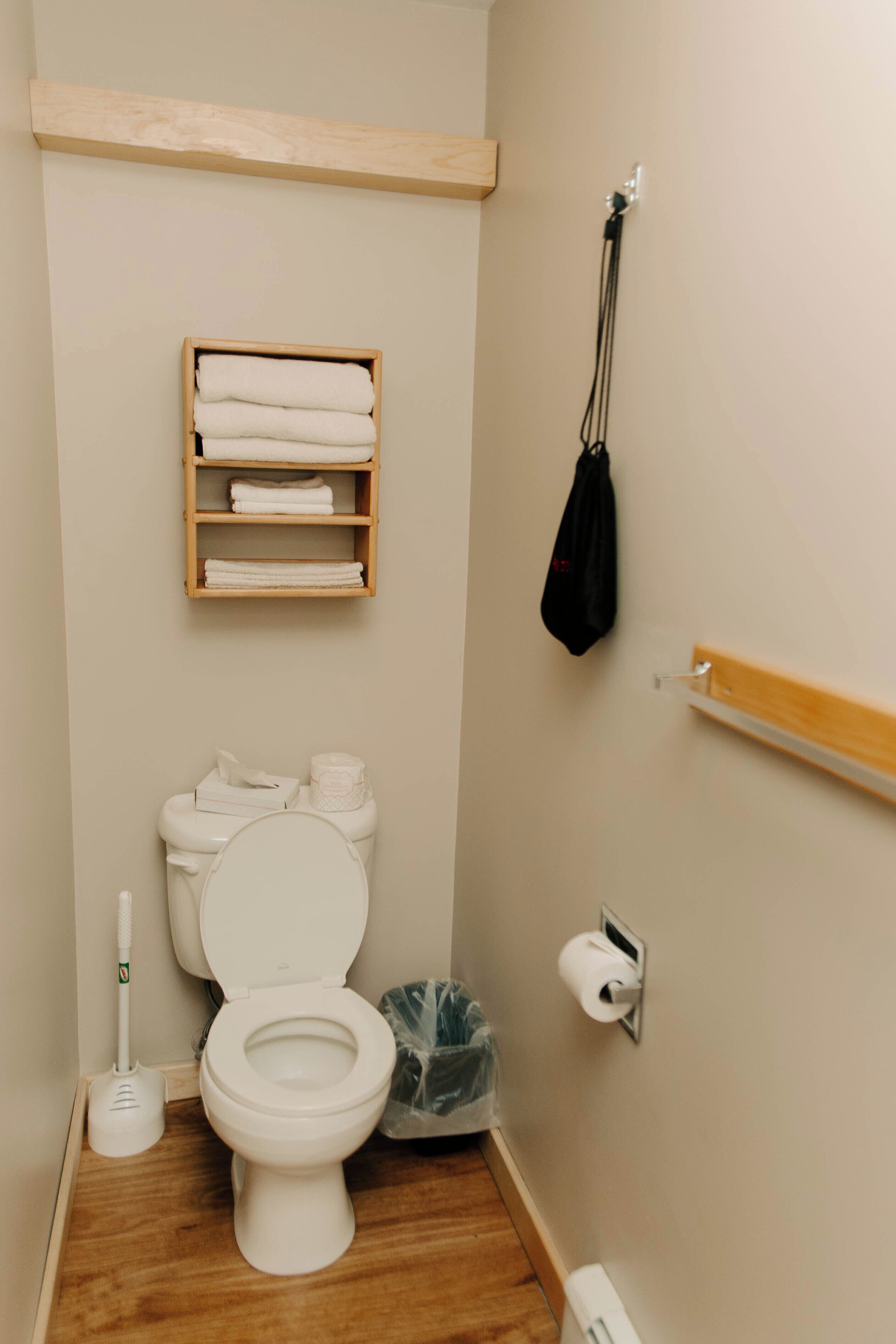 Een kleine badkamer met toilet, een plank met handdoeken, een prullenbak en een handdroger.
