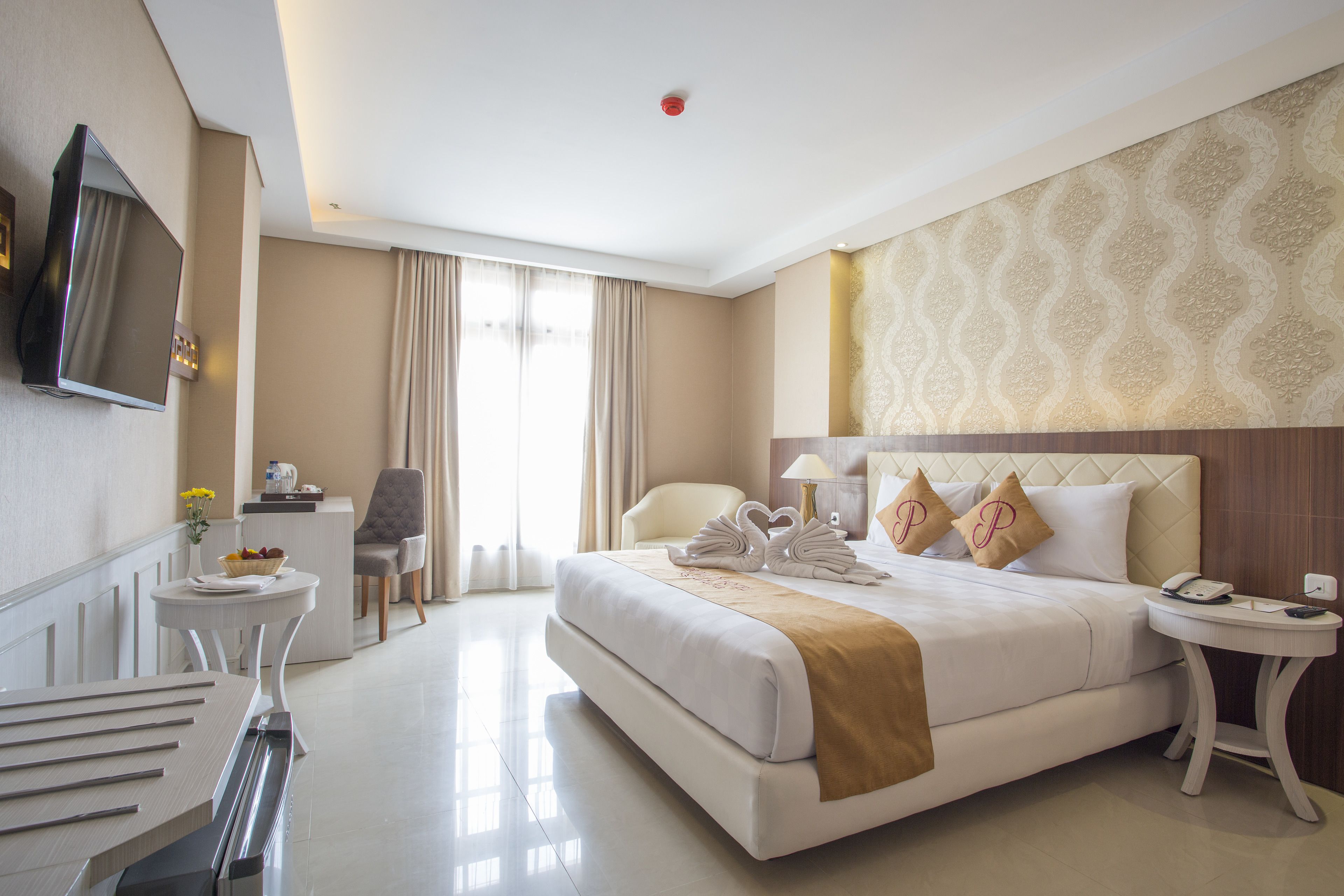 A hotel room with a large bed, a TV mounted on the wall, a desk with a lamp, and a chair.