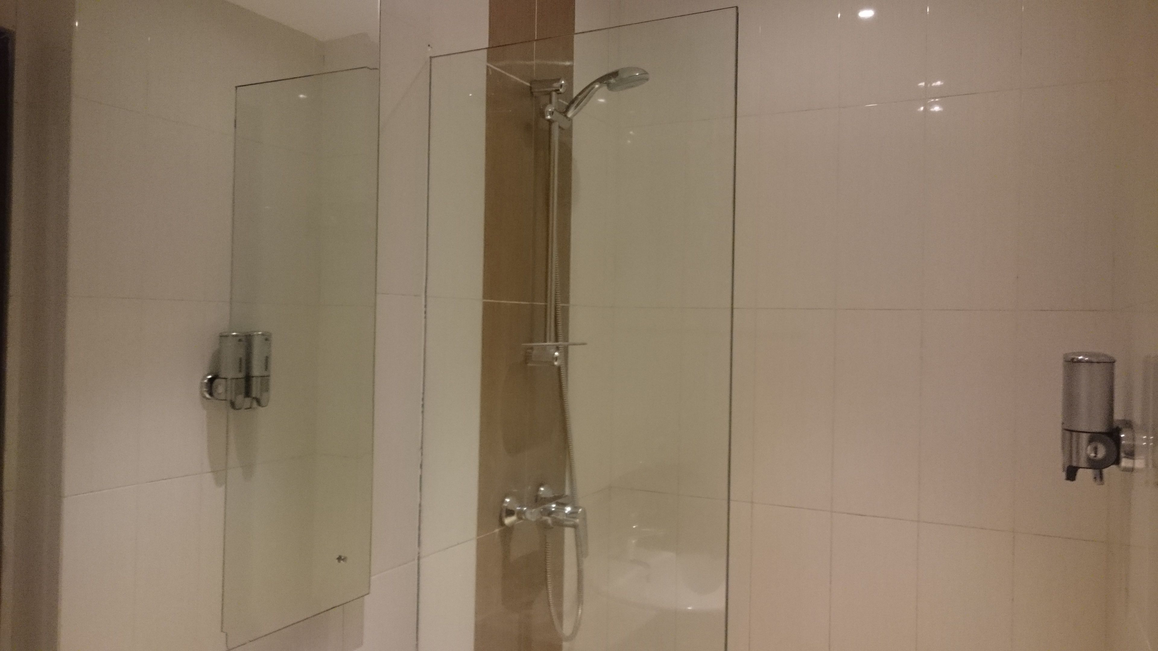 Een moderne badkamer met een douchecabine van glas, een handdouche en een wandmengkraan.