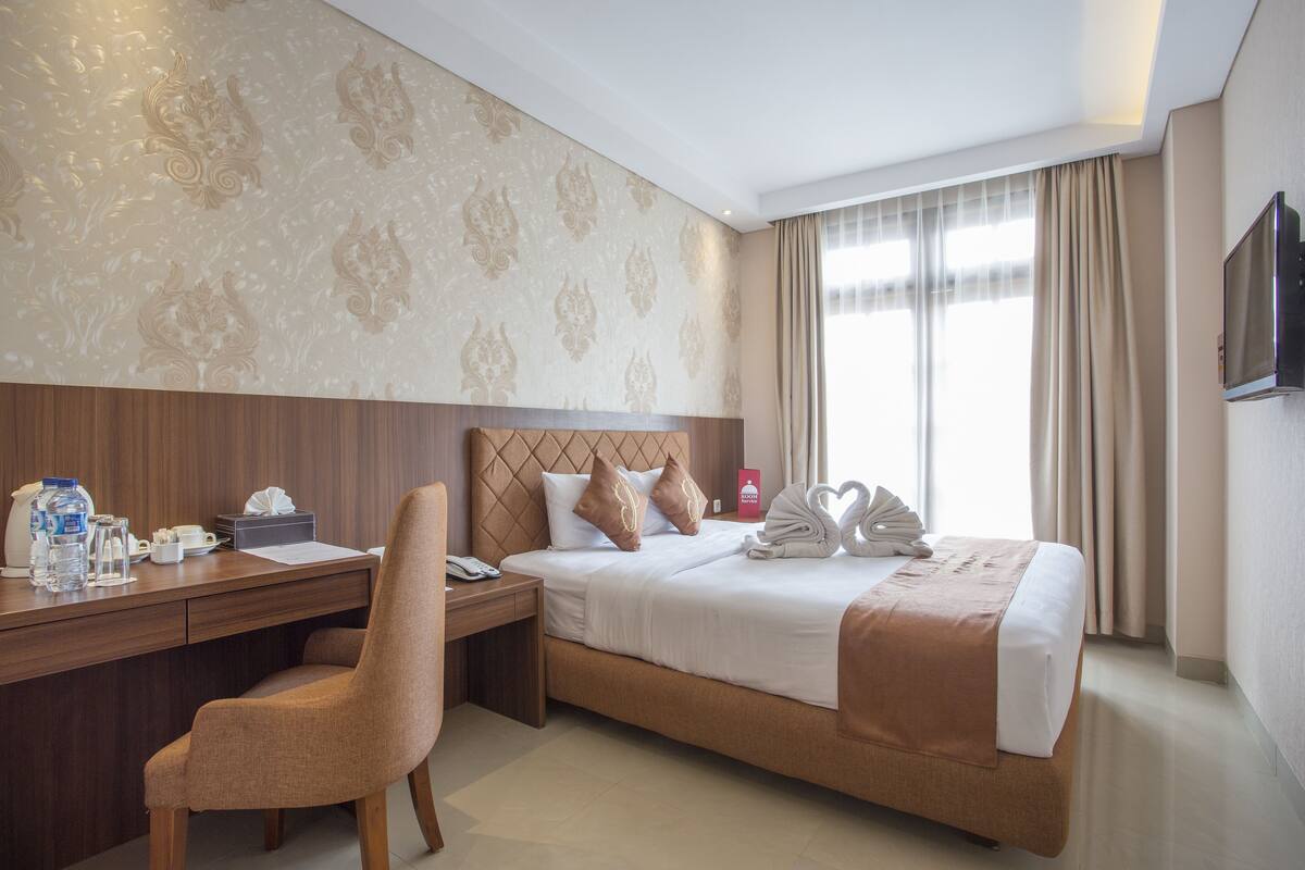 Une chambre d’hôtel avec un lit, un bureau, une chaise, une télévision et une fenêtre avec des rideaux.