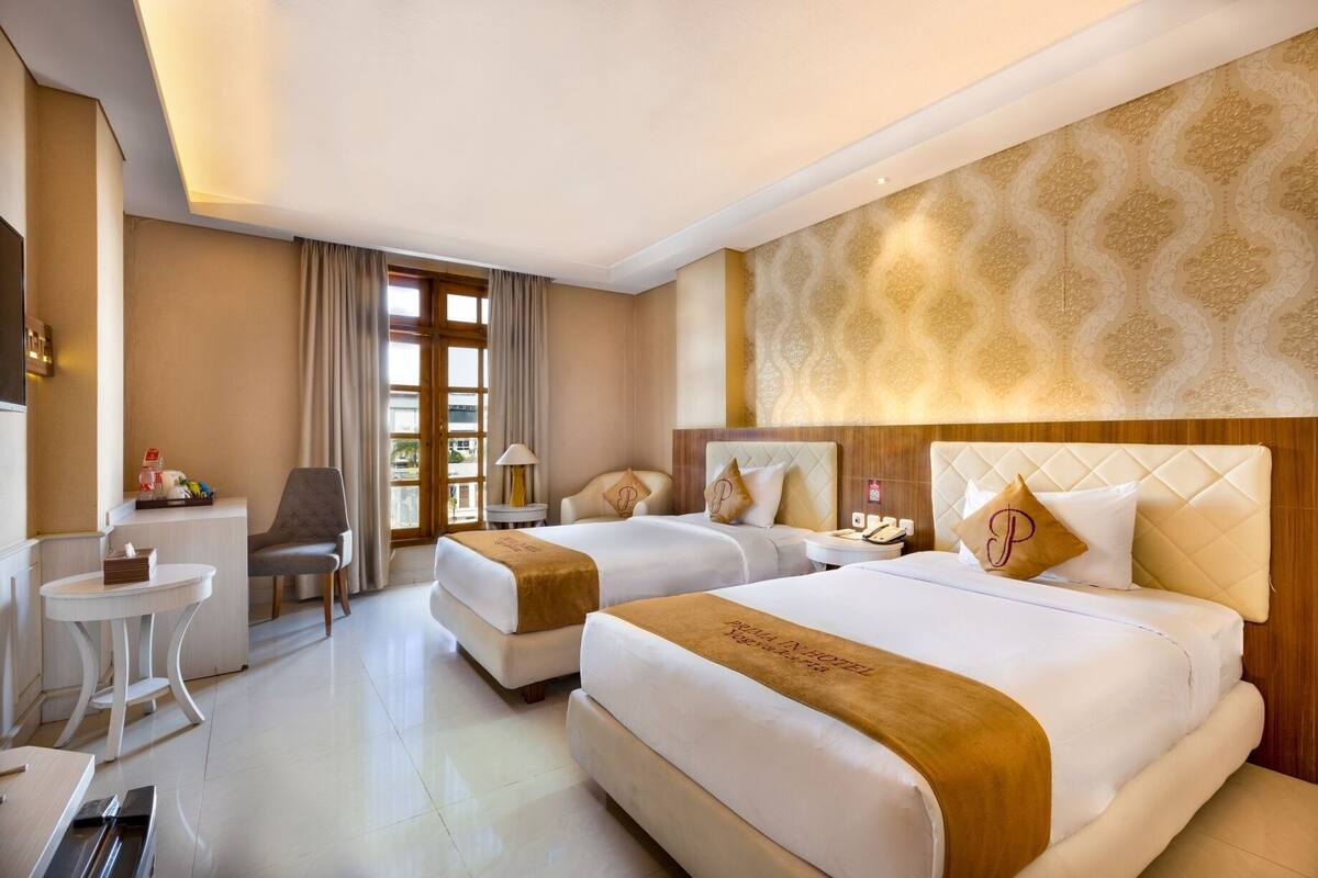 Une chambre d’hôtel avec deux lits, un bureau, une chaise et une fenêtre avec des rideaux.