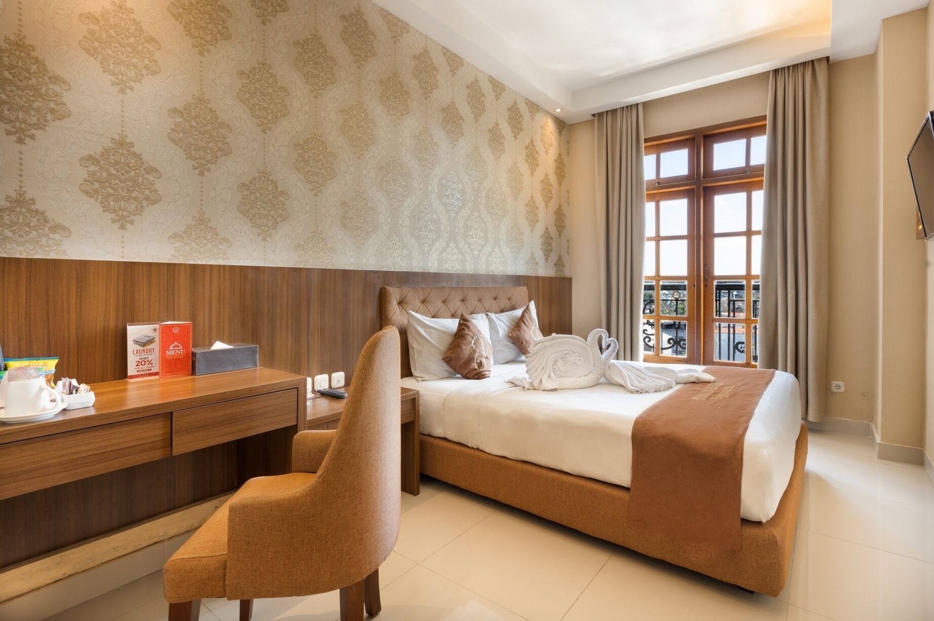 A hotel room with a bed, a desk, a chair, and a window with curtains.