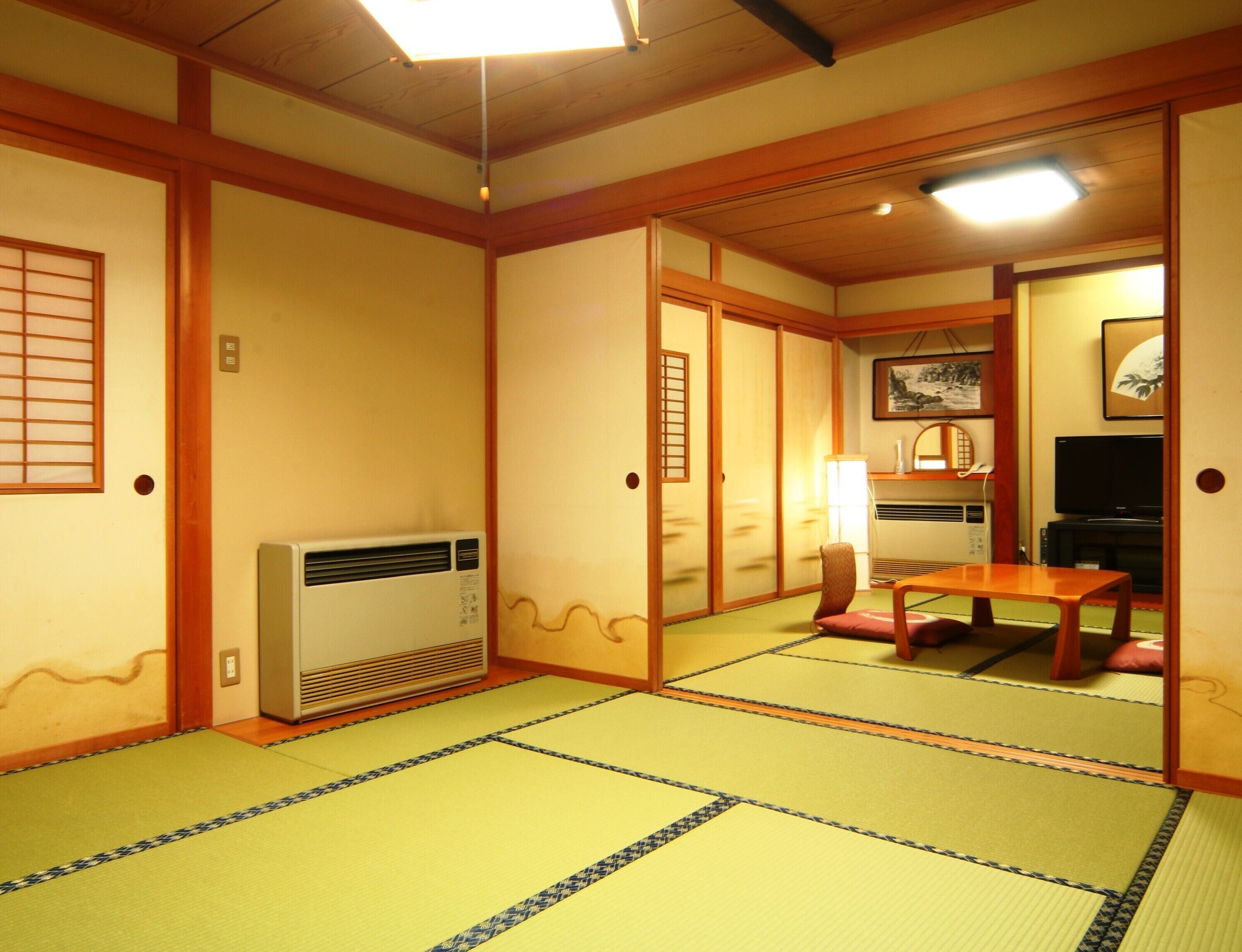 A traditional Japanese room with tatami flooring, a heater, a television, and sliding doors.