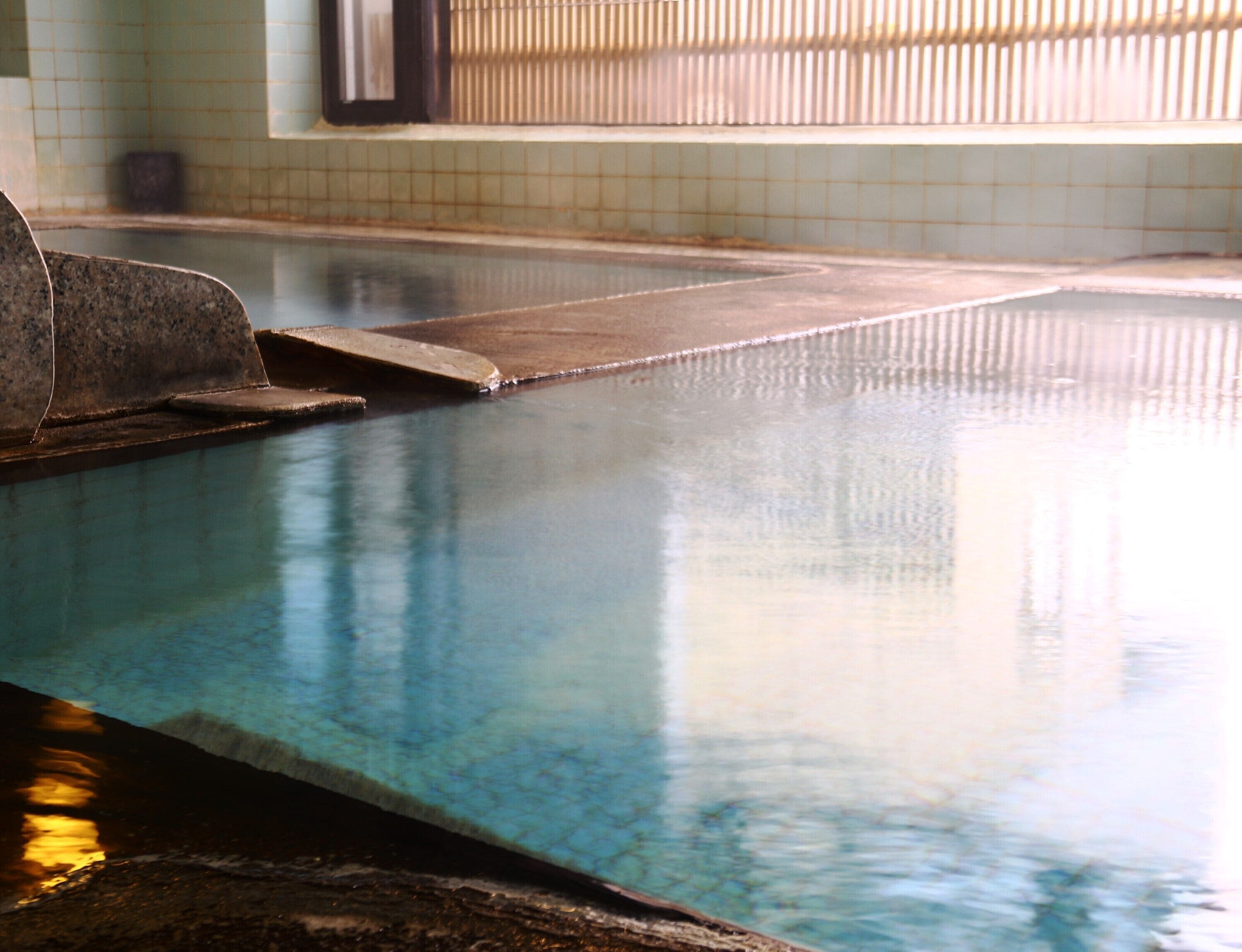 A swimming pool with clear water, tiled walls, and a wooden deck.