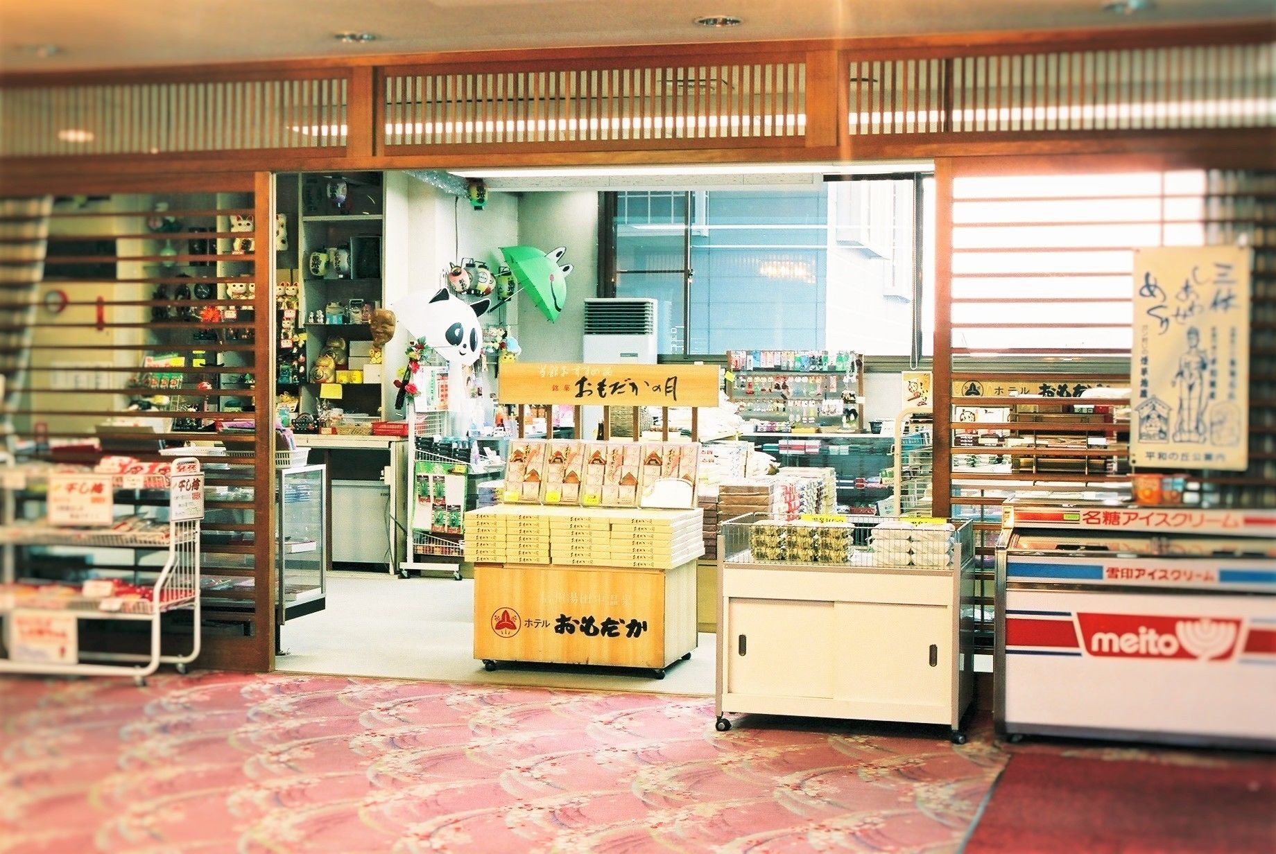 A small shop with shelves stocked with various items, a display counter with boxes, and a sign with Japanese characters.