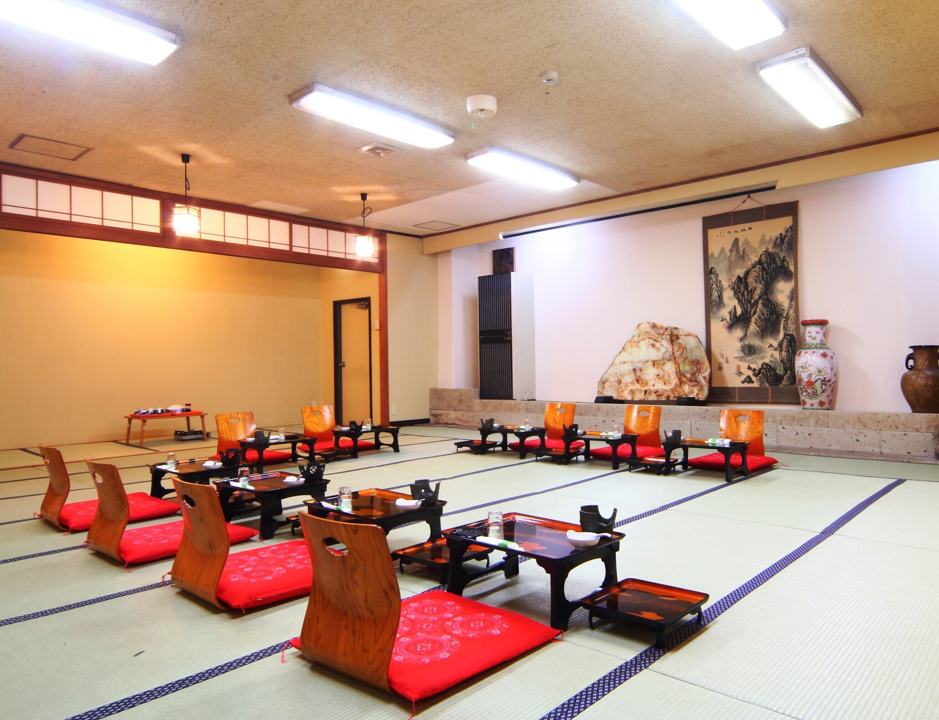 A traditional Japanese room with tatami mats, low wooden tables, and red cushions.