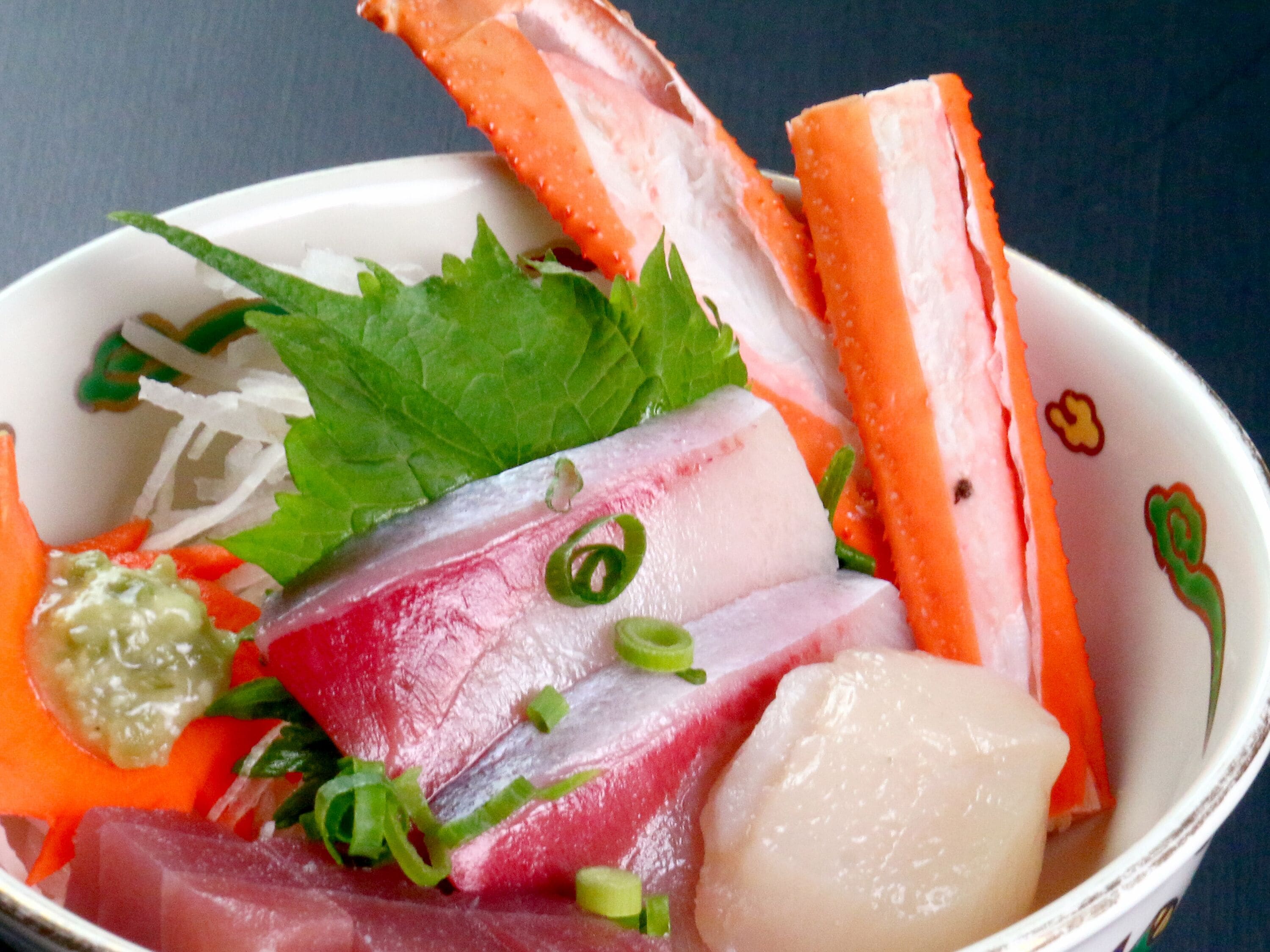 Un bol de sashimi composé de différentes tranches de poisson, garni d’oignons verts et de radis daïkon râpé.