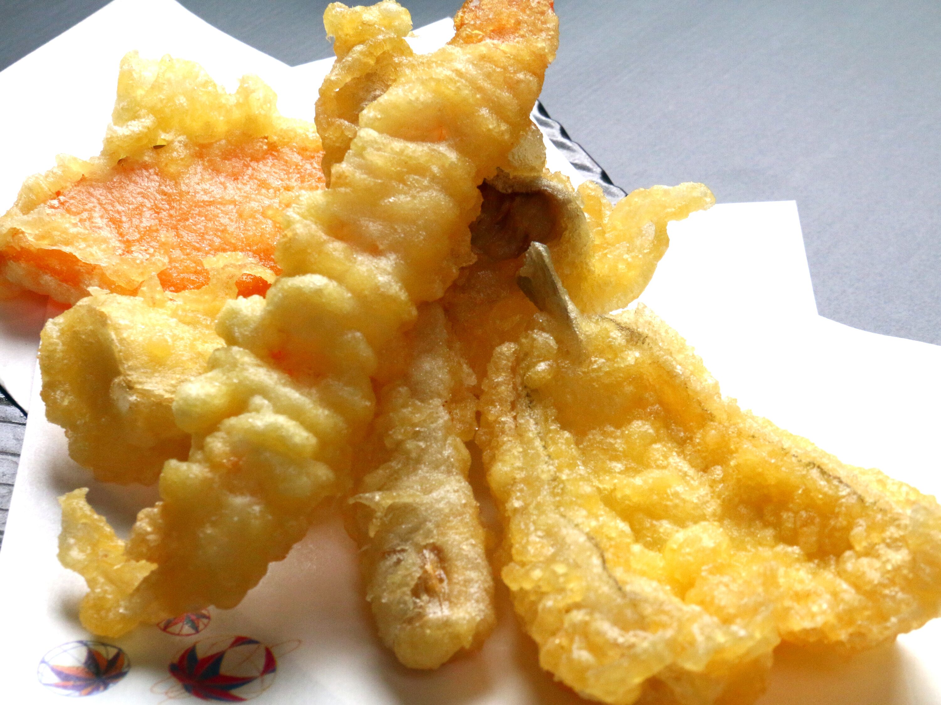 A close-up of a piece of fried food, possibly tempura, with a crispy, golden-brown exterior.