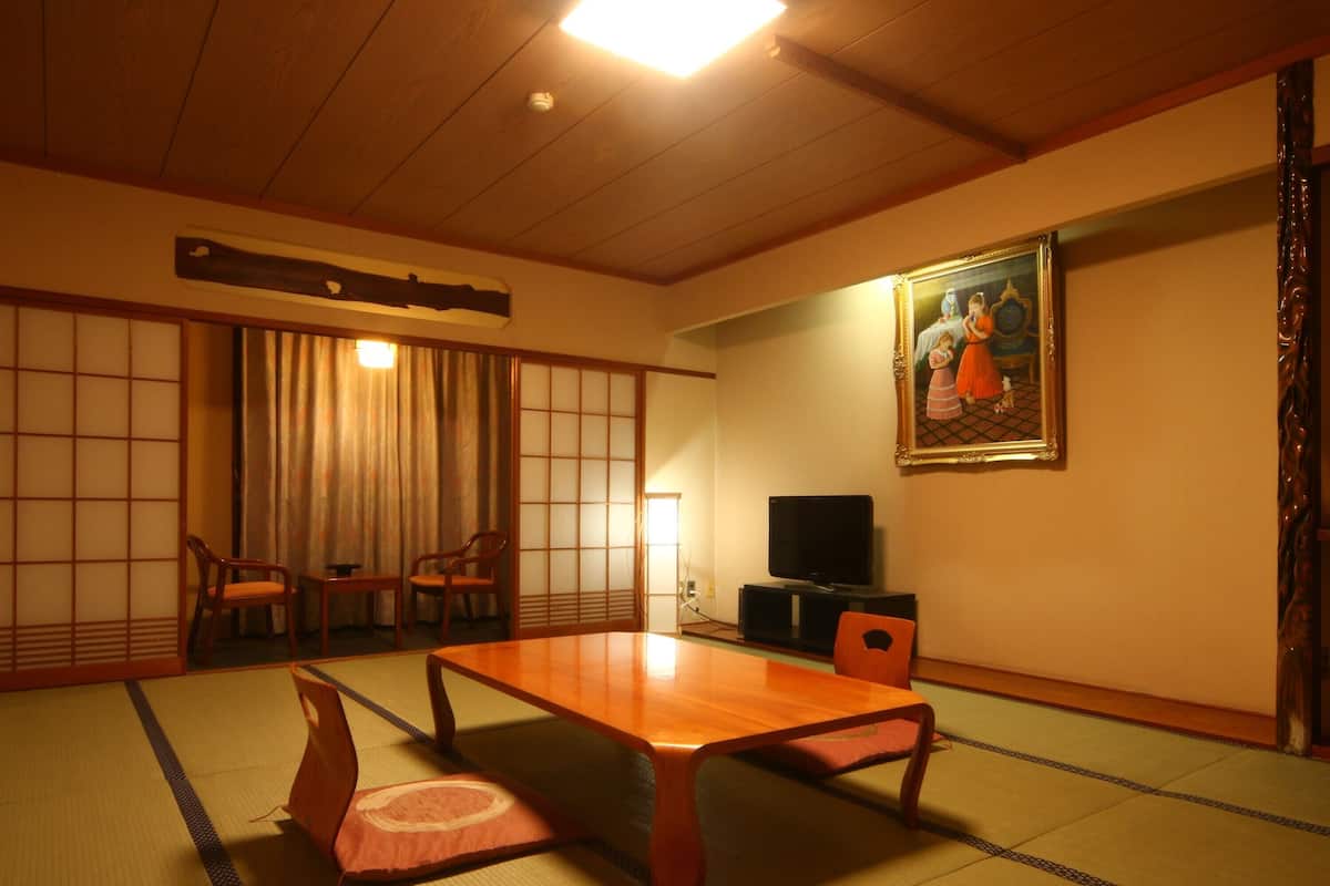 A traditional Japanese room with tatami flooring, a low table, two chairs, a television, and a painting on the wall.
