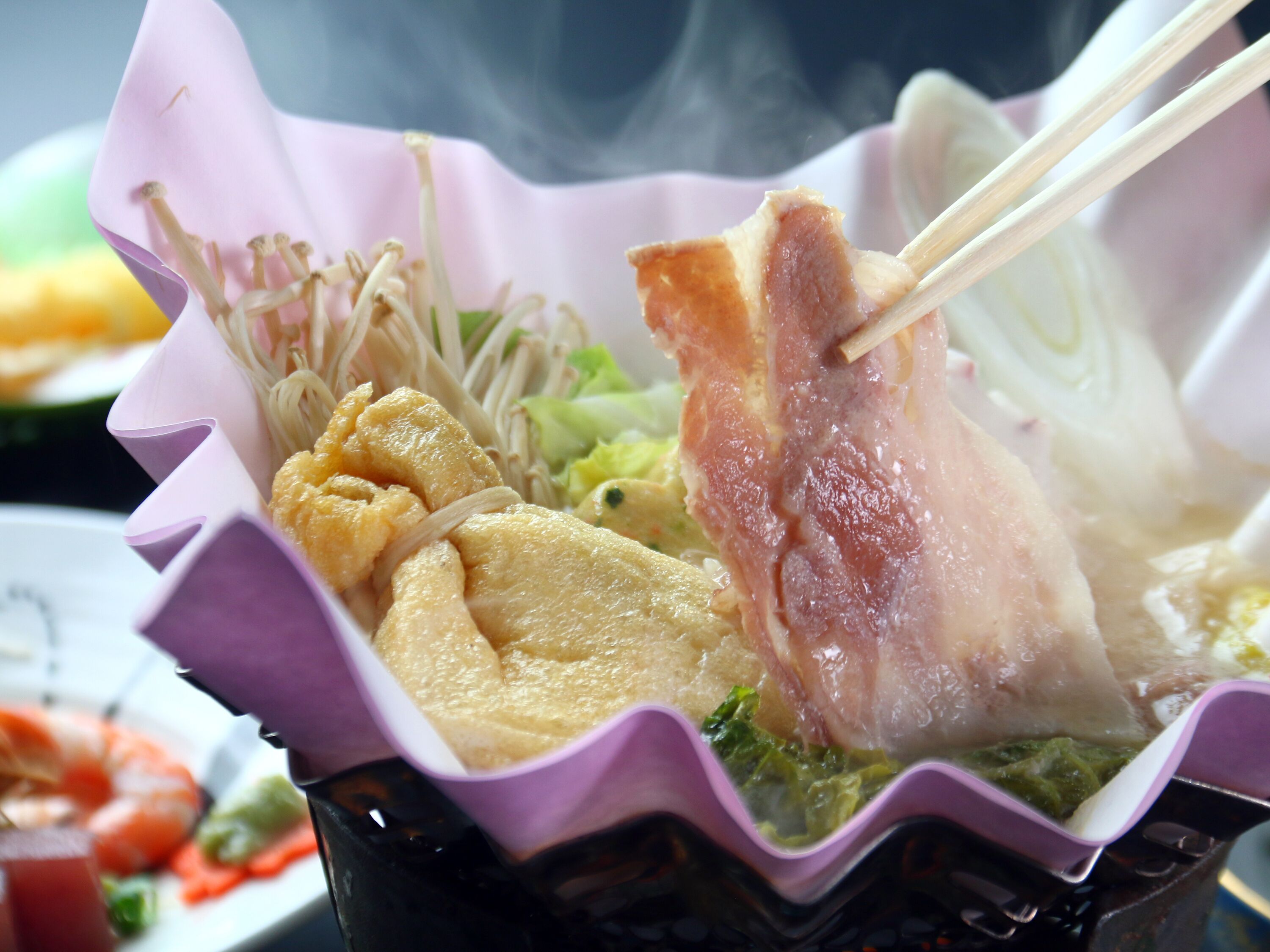A close-up of a meal with various dishes including noodles, vegetables, and meat, served in a purple container.