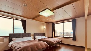 Habitación de hotel con dos camas, suelo de madera, ventanas amplias y una lámpara en el techo.