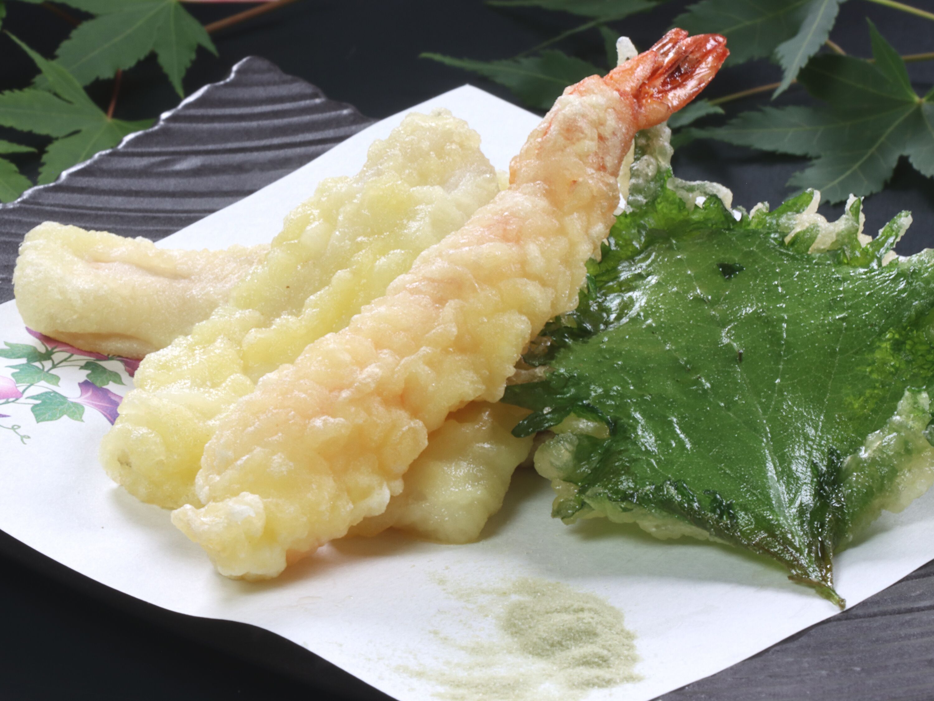 Un plato con dos camarones fritos en tempura y una alga.
