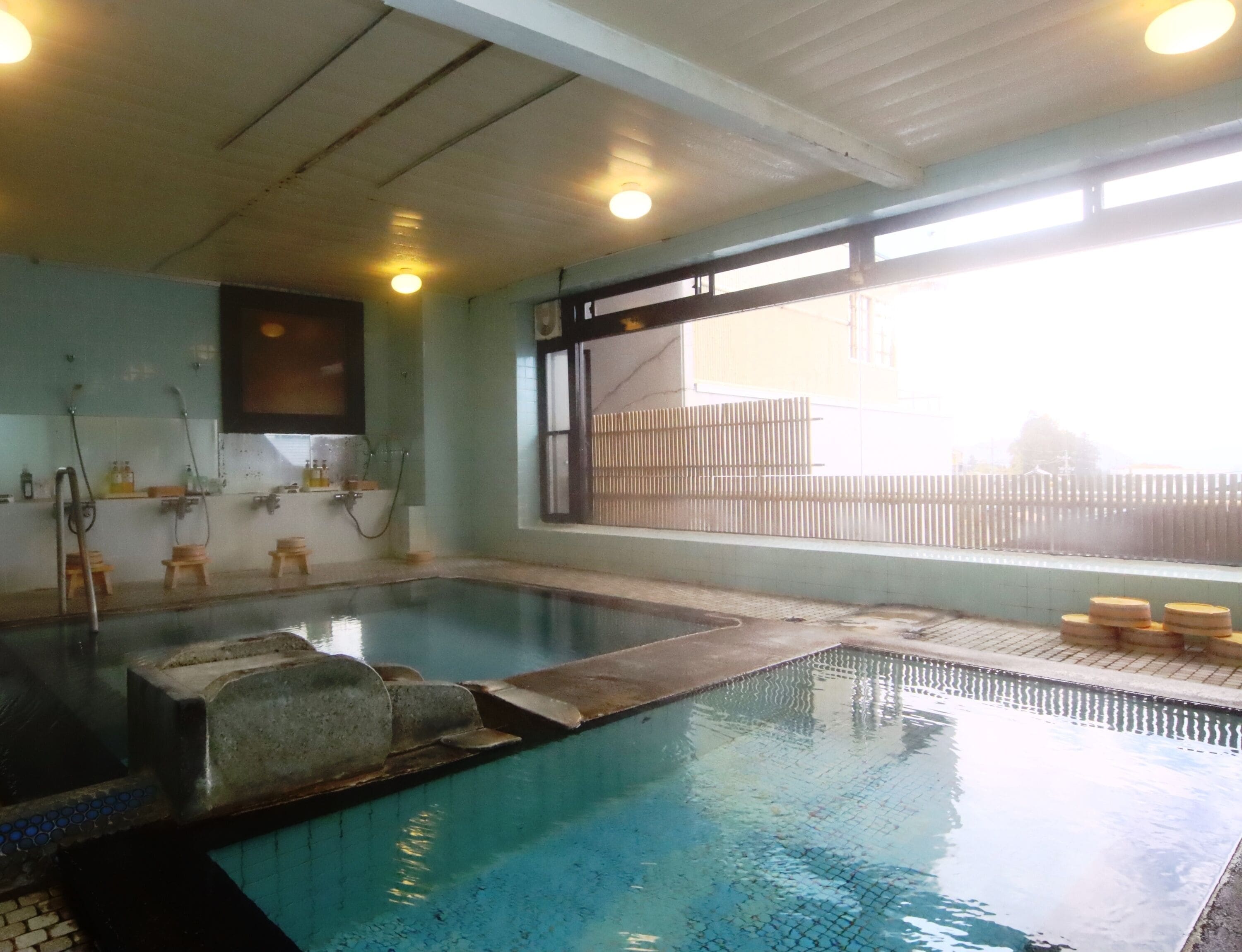 Une piscine avec un sol carrelé, une terrasse en bois et une fenêtre donnant sur une clôture.