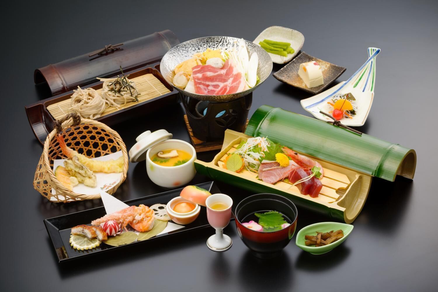A variety of Japanese dishes including sushi, sashimi, and tempura, arranged on a black tray.