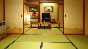 Una habitación japonesa tradicional con suelo de tatami, una mesa baja con cojines, televisión y un refrigerador pequeño.