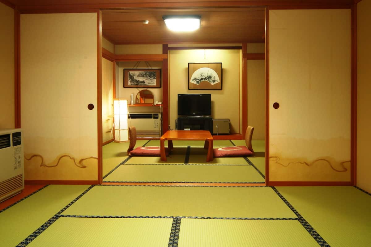 A traditional Japanese room with tatami flooring, a low table with cushions, a television, and a small refrigerator.