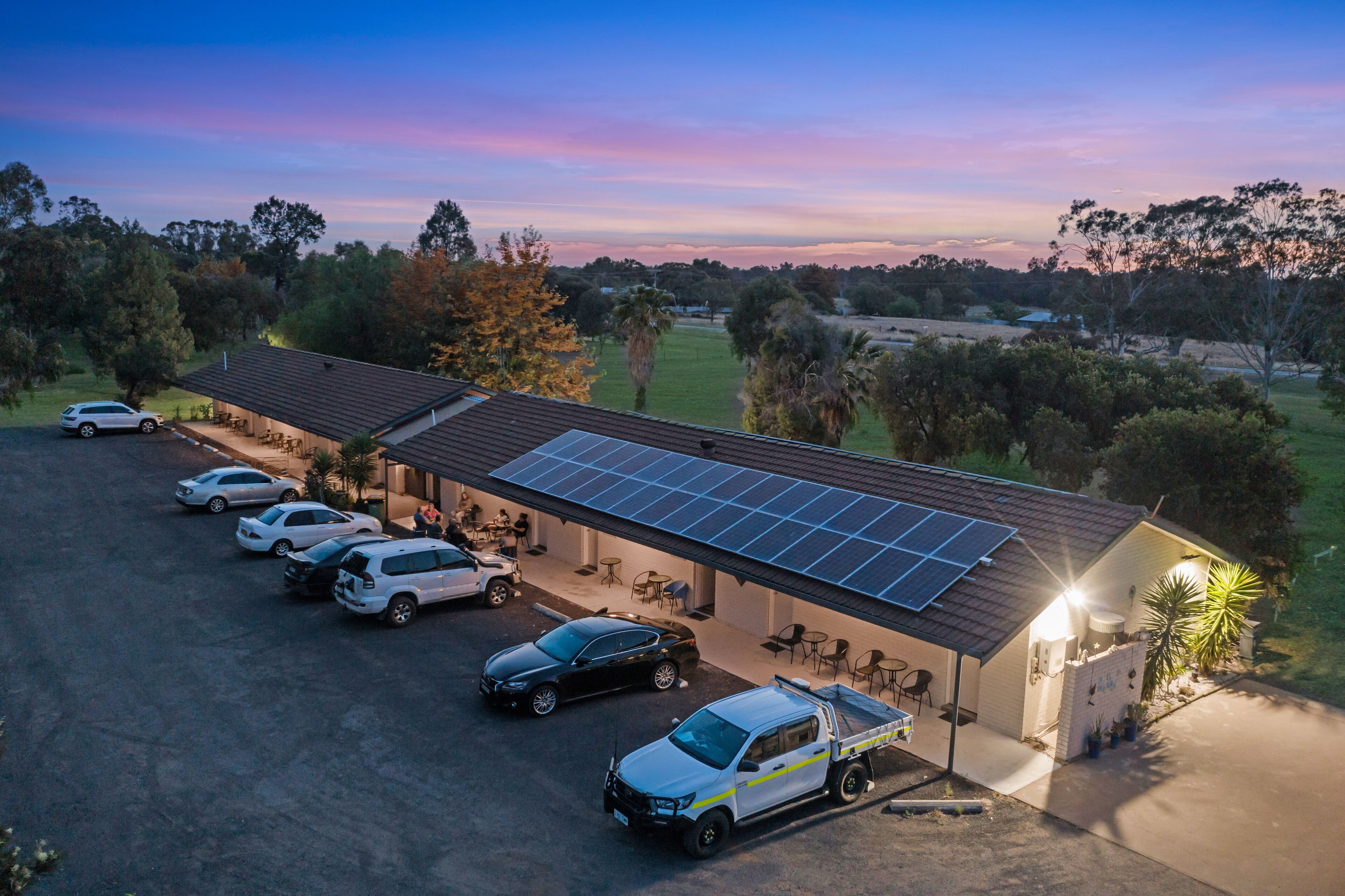 Um edifício com telhado em painéis solares, área de estacionamento coberta e um pequeno jardim.