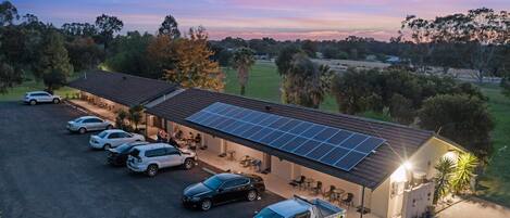 Um edifício com telhado em painéis solares, área de estacionamento coberta e um pequeno jardim.