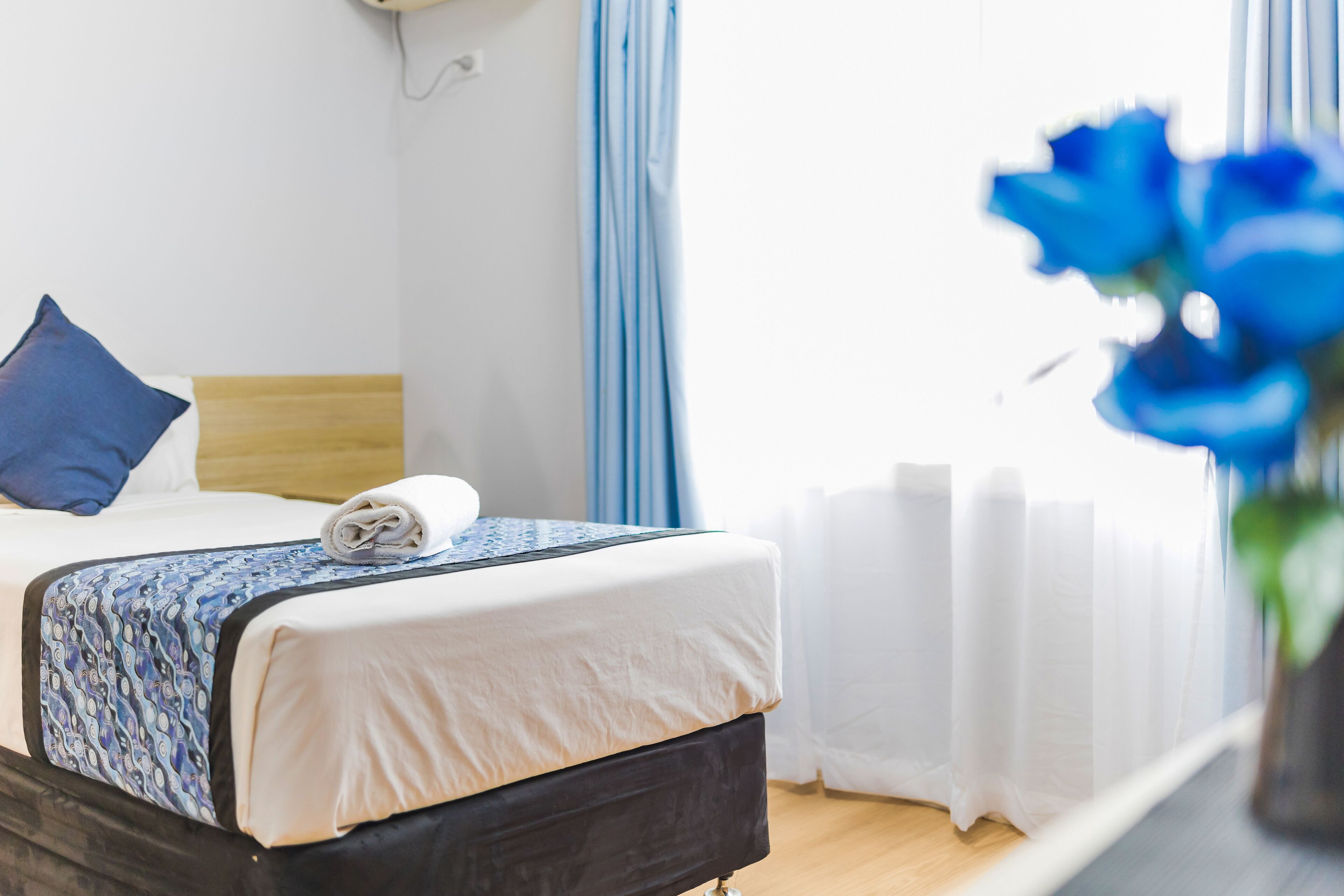 A neatly made bed with a patterned bedspread, a blue pillow, and a rolled towel on the headboard.