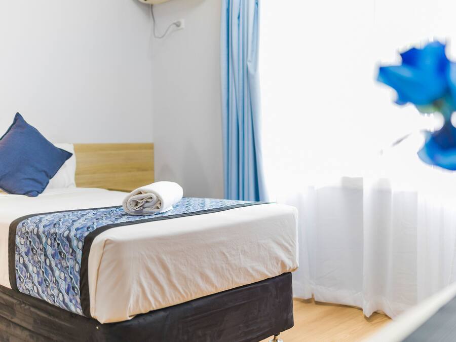 A neatly made bed with a patterned bedspread, a blue pillow, and a rolled towel on the headboard.