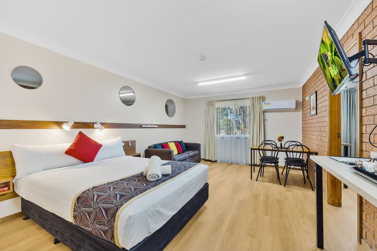 A hotel room with a bed, a desk, a TV, and a dining area.