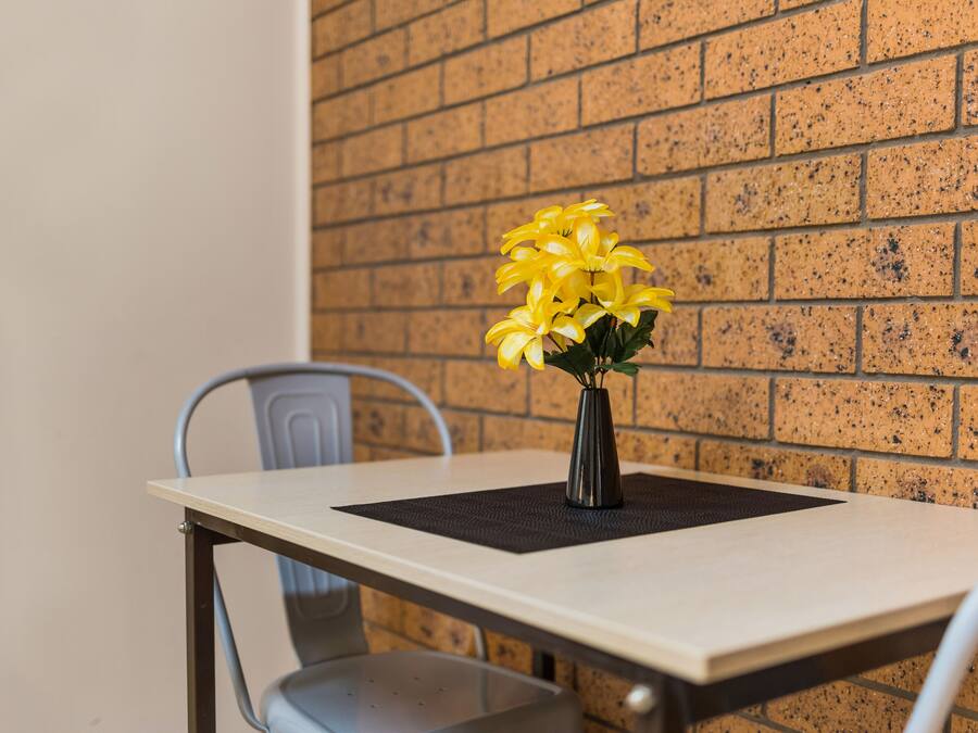 Een tafel met een vaas gele bloemen, een stoel en een bakstenen muur op de achtergrond.