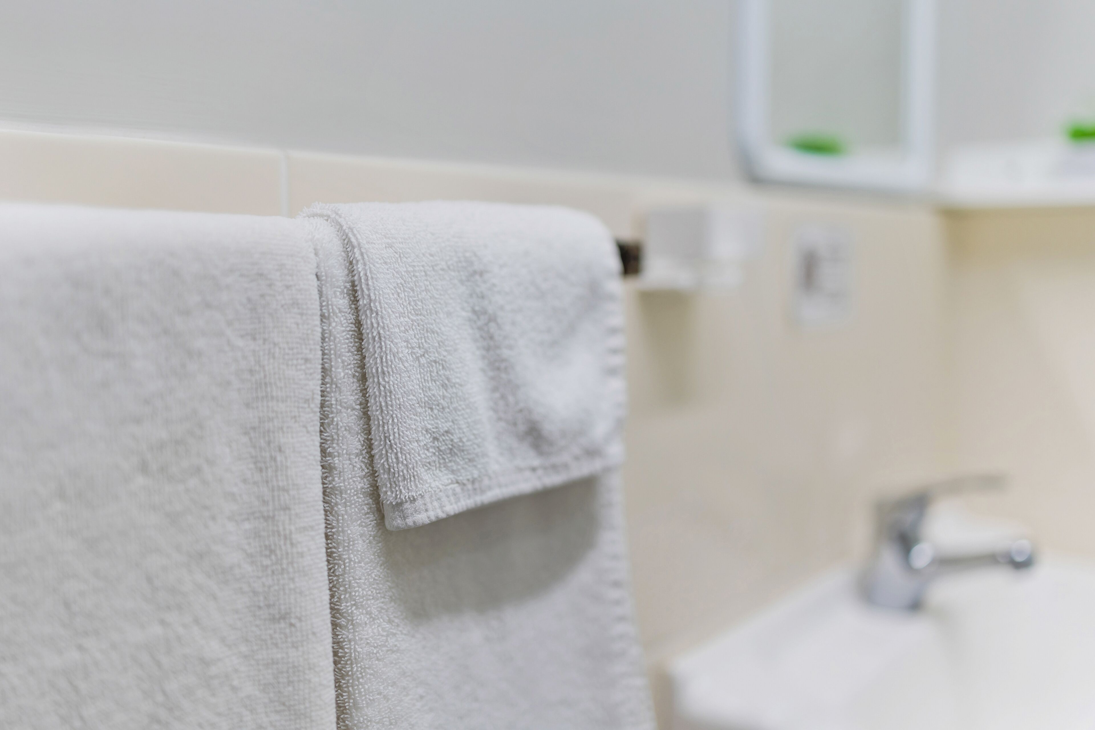 Un baño con una toalla blanca colgada en un perchero, un lavamanos y un espejo sobre él.