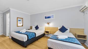 A hotel room with two beds, a wooden headboard, a nightstand, a bedside table, and a wall-mounted air conditioner.