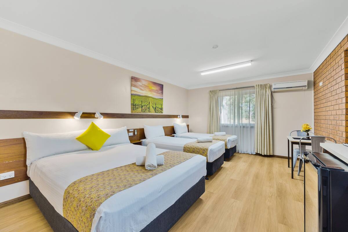 A hotel room with three beds, a desk, and a window with curtains.