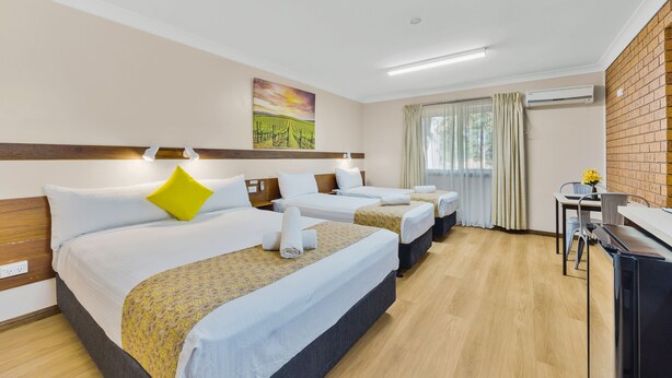 Una habitación de hotel con tres camas, un escritorio y una ventana con cortinas.