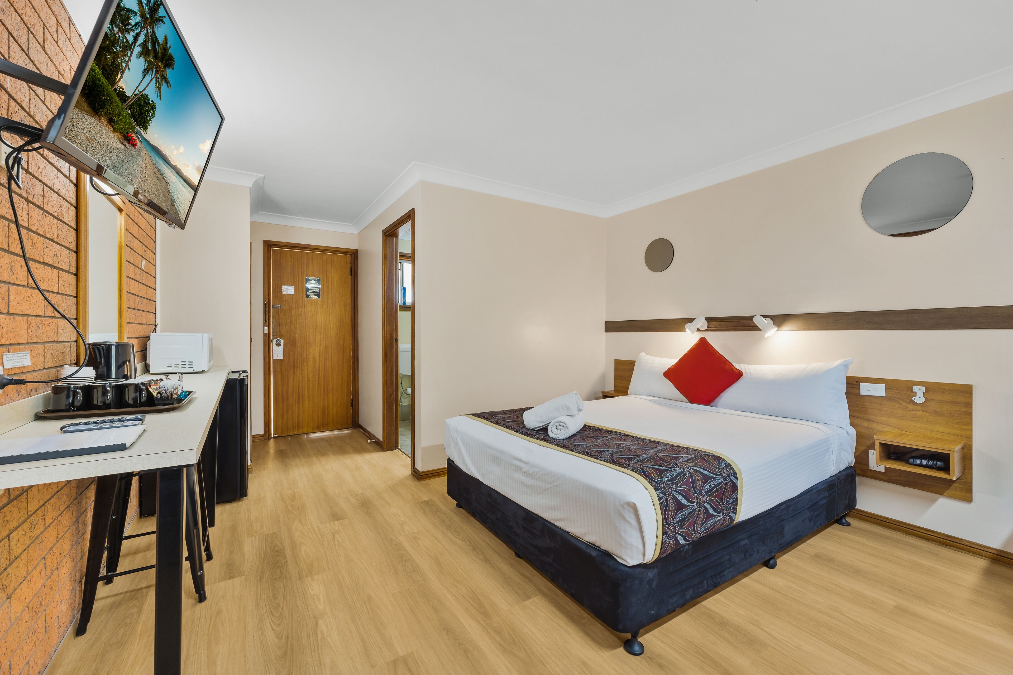 A hotel room with a bed, desk, and a TV mounted on the wall.