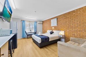 A modern hotel room with a brick accent wall, a flat-screen TV, a desk with a computer, a bed with a pillow, and a chair.