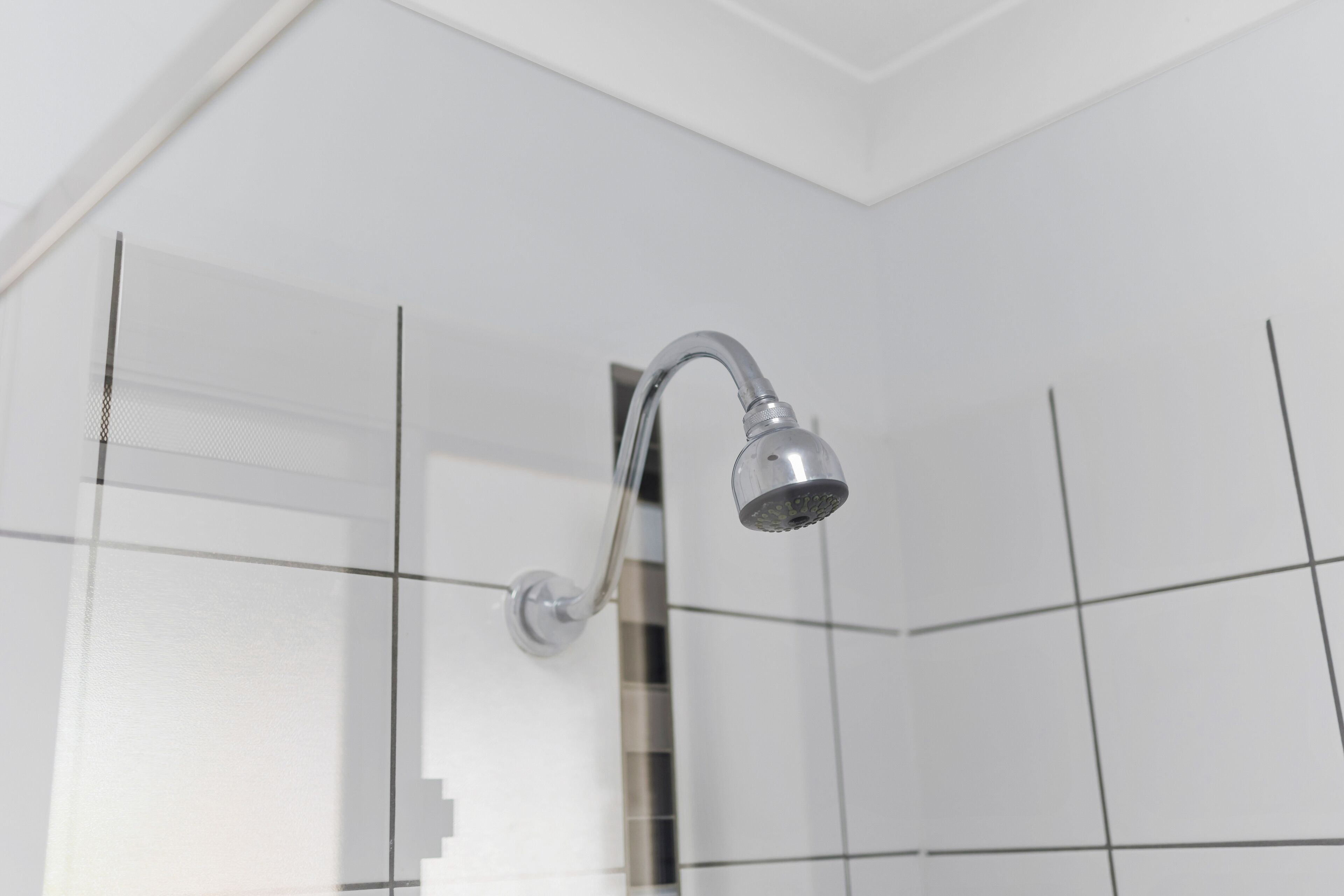 A shower with a chrome head and a wall-mounted handle.