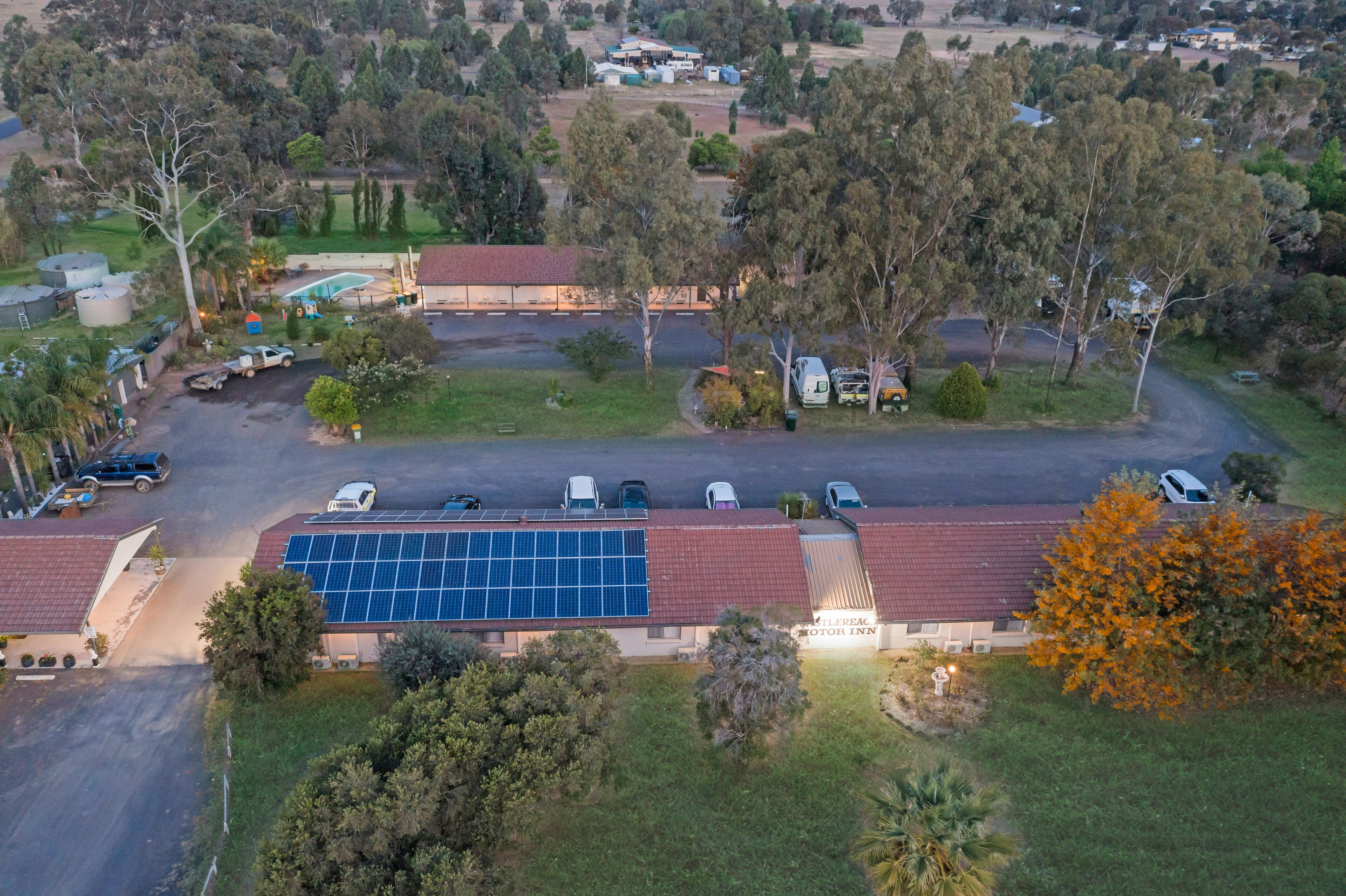 Vista aérea de un motel con techo de paneles solares, rodeado de árboles y un estacionamiento.