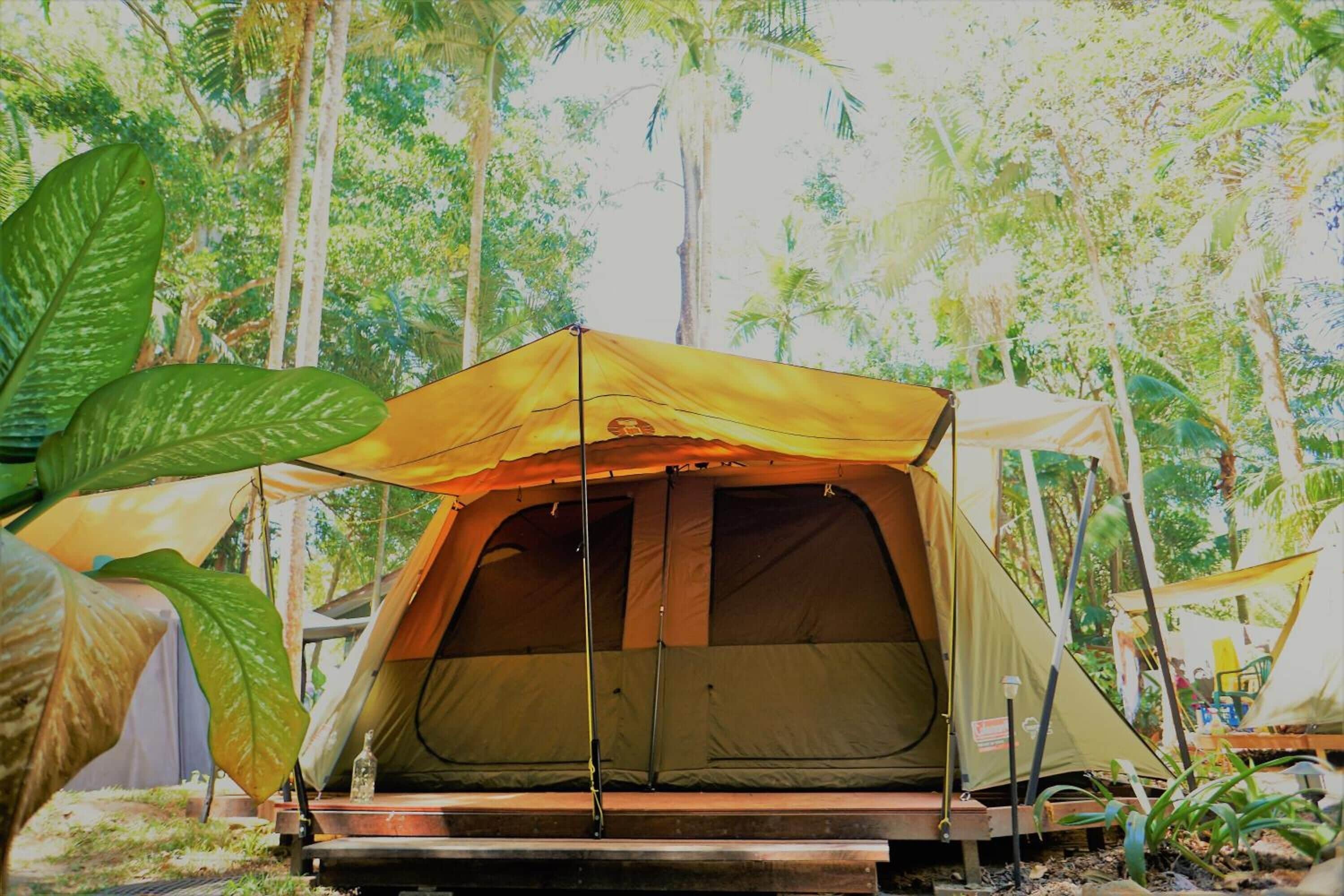 A tent set up in a forested area with a table and chairs nearby.