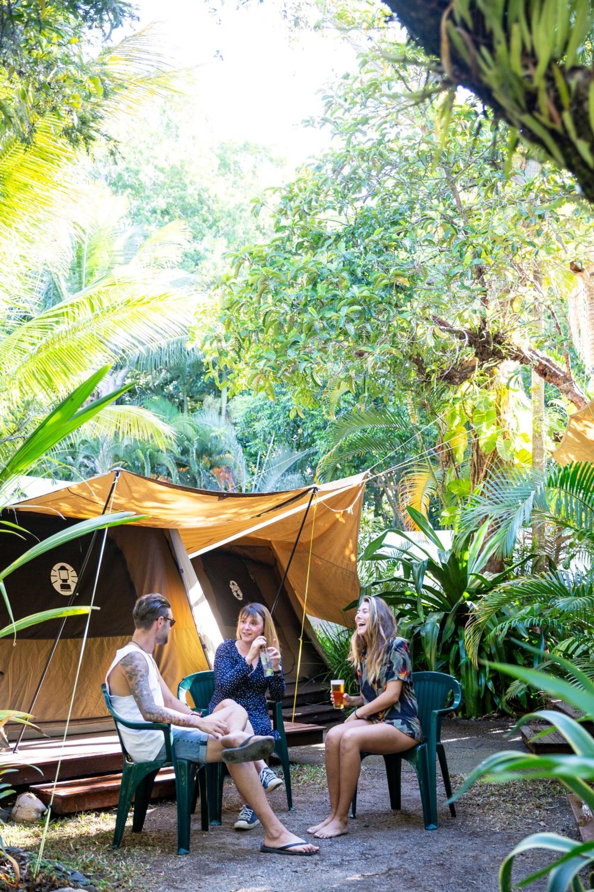 A tent set up in a lush, green environment with a few chairs around it.