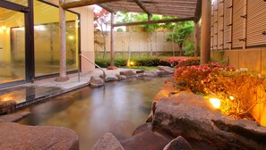 Un jardín interior tranquilo con fuente de agua, senderos de piedra y una pérgola de madera.