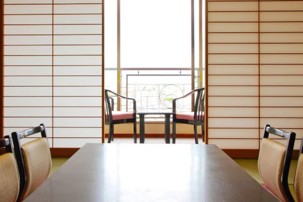 Una habitación con una mesa larga y cuatro sillas, una ventana con vistas y una puerta corredera con diseño de cuadrícula.