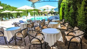 Outdoor seating with tables and chairs, a pool, and umbrellas in a resort setting. - Valentino Hotel (Rhodes)