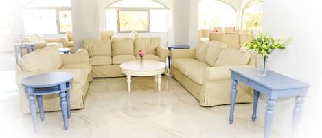 A spacious living room with a beige sectional sofa, a round coffee table, and a blue side table.