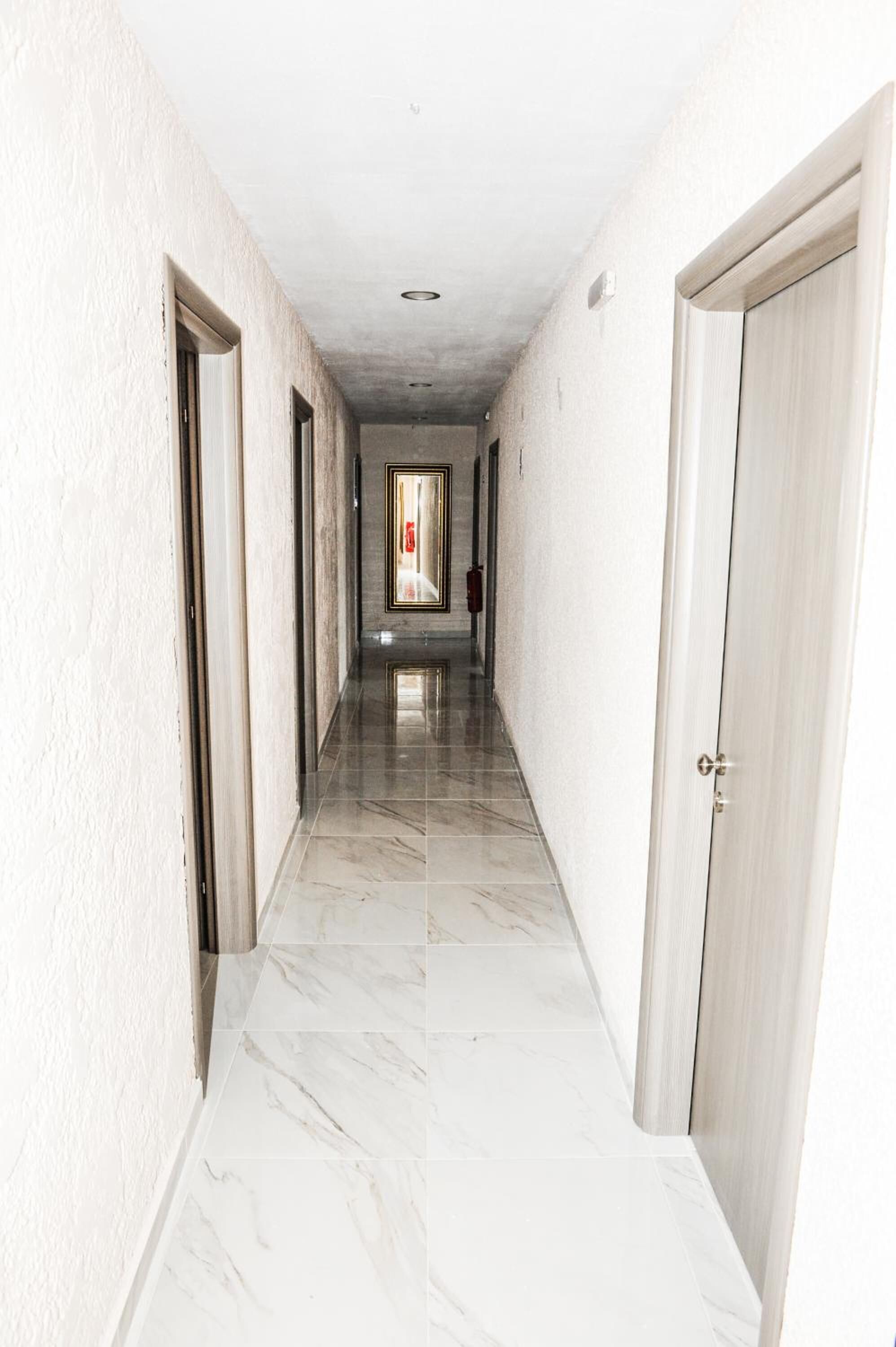 Un pasillo con paredes blancas y suelo de mármol, que conduce a una puerta al final.